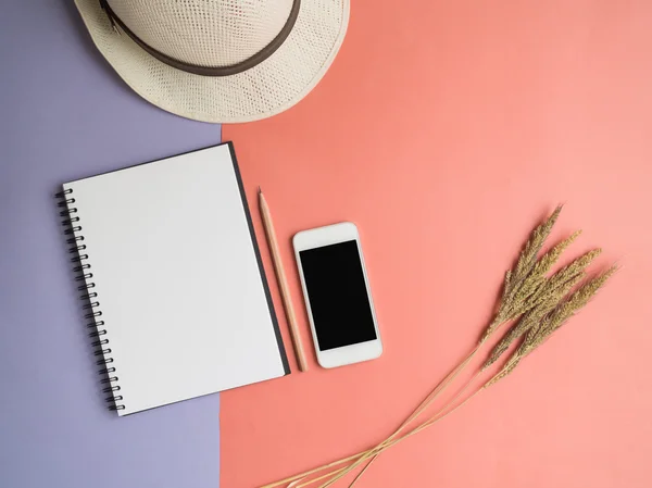 Top view of notebook, smartphone, hat, dried flower on violet pu