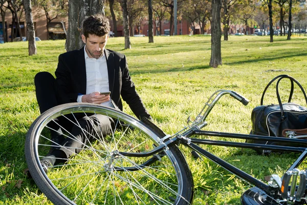 Man with bicycle looks at the telephone in the park