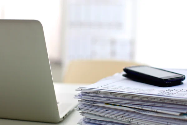 A stack of papers on the desk with a computer
