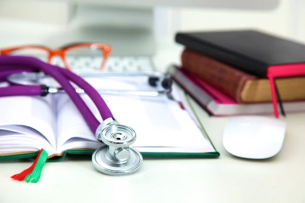 Stethoscope lying on a notebook computer in the background and books