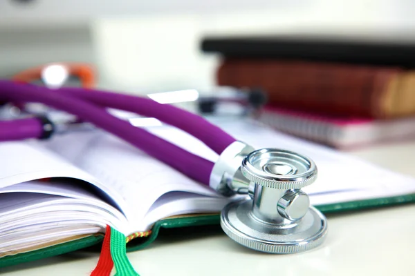 Stethoscope lying on a notebook computer in the background and books