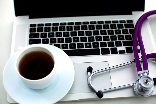 Medical stethoscope lying on a computer keyboard, a cup of coffee
