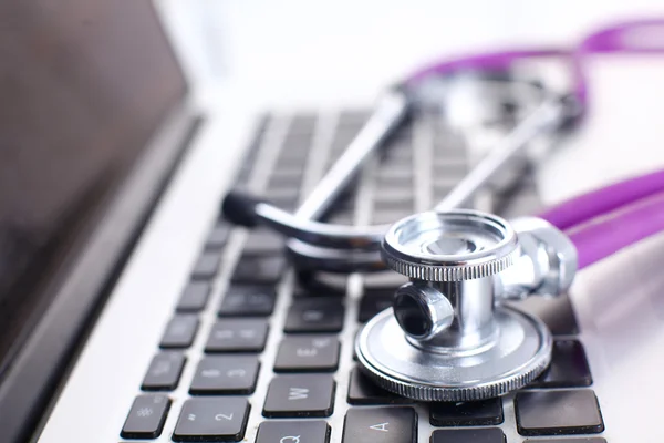 A medical stethoscope near a laptop on a wooden table, on white