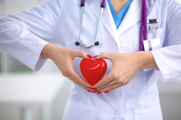 Young woman doctor holding a red heart, in office