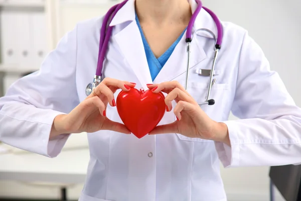 Young woman doctor holding a red heart, in office