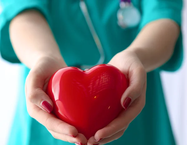 Young woman doctor holding a red heart, in office