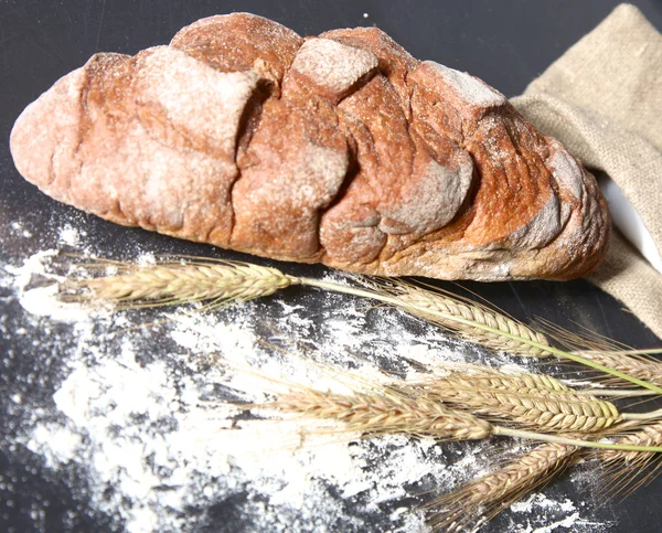 Rustic crusty bread and wheat ears on a dark wooden table