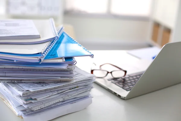 Laptop with stack of folders on table on white background