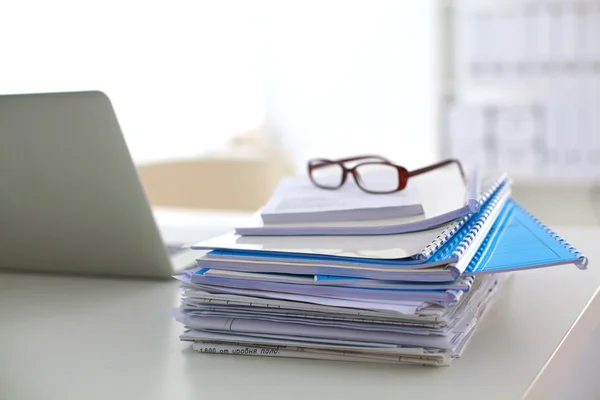 Laptop with stack of folders on table on white background