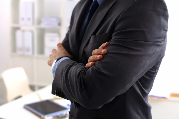 Smiling middle aged businessman in a shirt and tie standing in a modern office building with his arms crossed