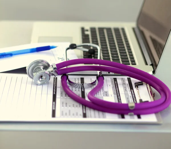 A medical stethoscope near a laptop on a wooden table, on white