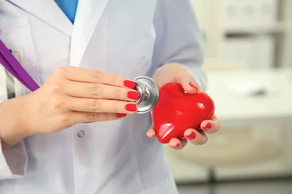 Young woman doctor holding a red heart, in office