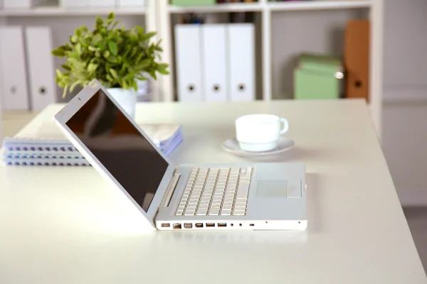 Close up view of a work desk interior with a laptop computer, a cup of coffee and white curtains on a sunny day