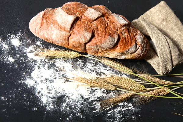 Rustic crusty bread and wheat ears on a dark wooden table