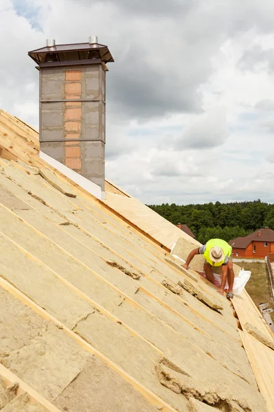 Roofer builder worker installing roof insulation material (rockwool) on new house under construction