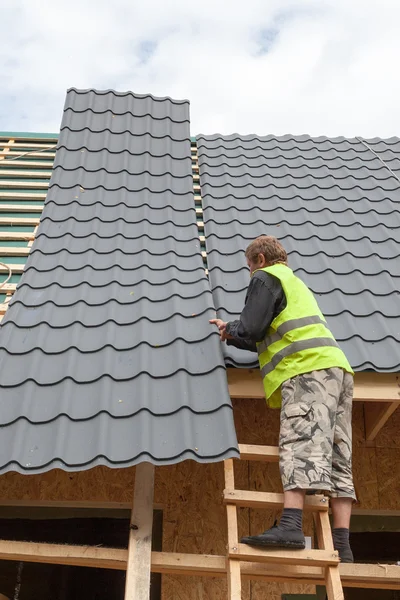 Roofer worker installing a metal tile on a new wooden house