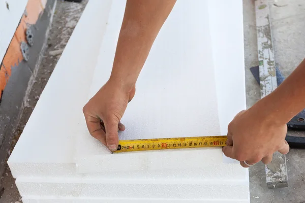 Thermal insulation house foundation walls with styrofoam boards. Worker use ruller to measure the  correct length of styrofoam