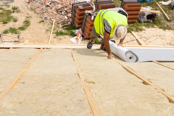 Roof insulation. Worker laying roofing membrane over insulation layer (rockwool)