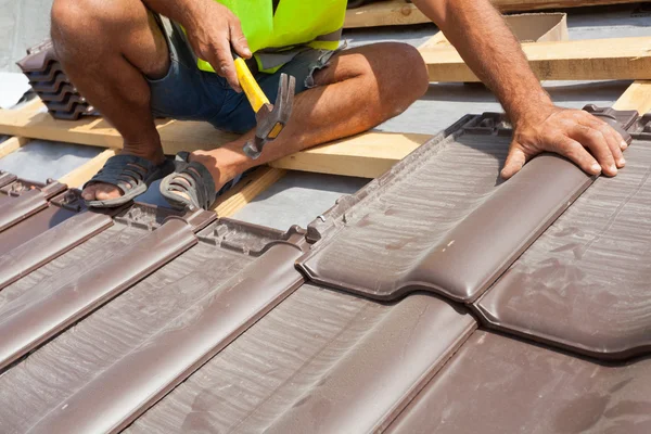 Hands of roofer laying tile on the roof. Installing natural red tile.