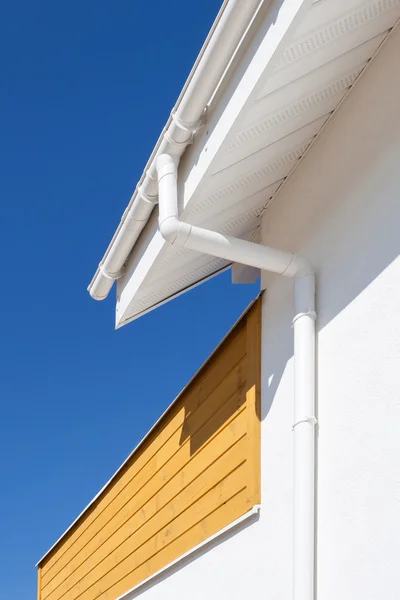 New rain gutter on a home with wooden panel against blue sky