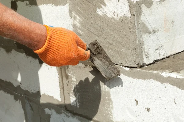 Bricklayer man worker in orange gloves installing aerated block with trowel