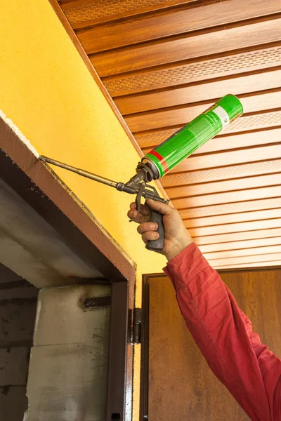 Construction builder works with polyurethane foam during frame insulation at door installation
