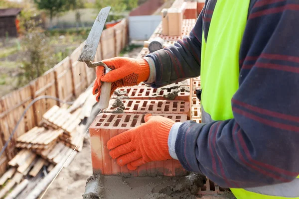 Construction mason worker bricklayer installing red brick with trowel putty knife outdoors