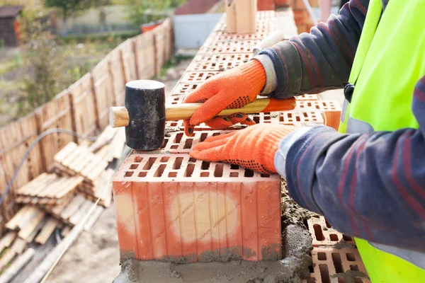 Construction mason worker bricklayer installing red brick with rubber mallet outdoors