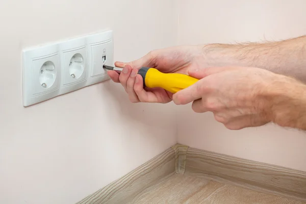 The hands of an electrician installing a wall power socket