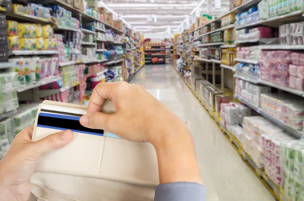 Hands pull credit card out of wallet with shopping mall blurred