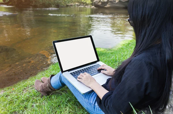 Blank screen laptop with girl sitting on grass field at riverside