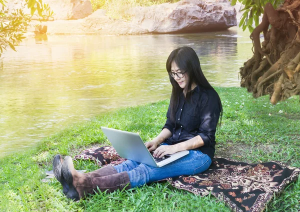 Blank screen laptop with girl sitting on grass field at riversid
