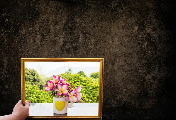 Hand hold picture frame of pink flowers and dark grunge wall