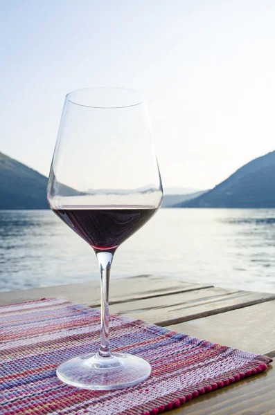 Close up view of the glass of red wine against blue sea and mountains during golden hour at sunset. Dinner on terrace in cafe.