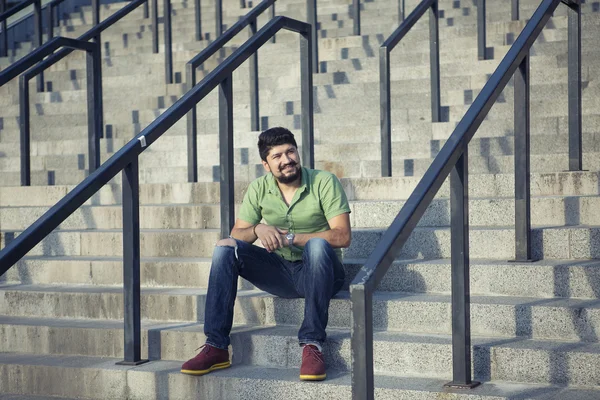 Bearded man with cool mustache in green shirt standing on the steps. Gesture serious stares.