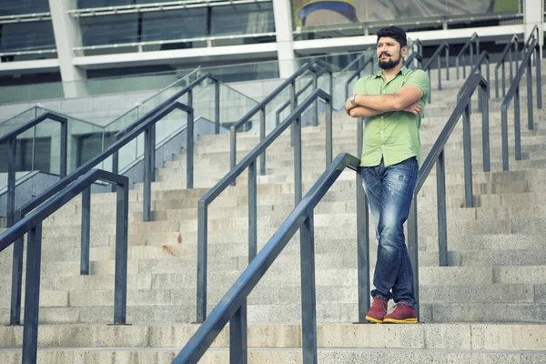 Bearded man with cool mustache in green shirt standing on the steps. Gesture serious stares.