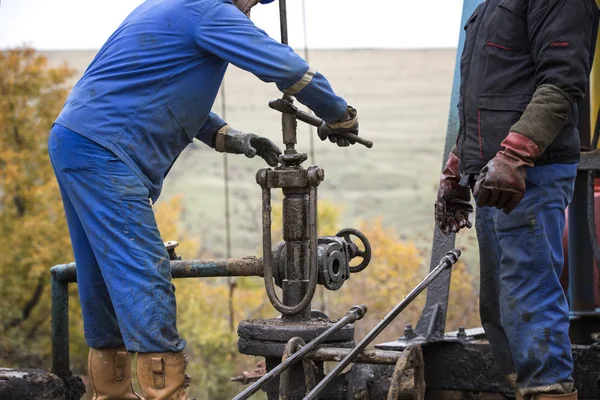 Oil workers check oil pump. Roustabouts doing dirty and dangerous work on an oil well servicing rig.
