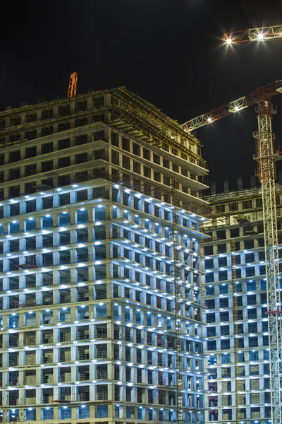 Lots of tower cranes build large residential buildings at night. buildings under construction with cranes and illumination at dark night. night shot of construction equipment at building site.