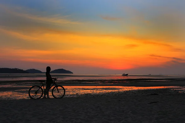 Silhouette of lonely unidentified girl with bike on beach with sunset light