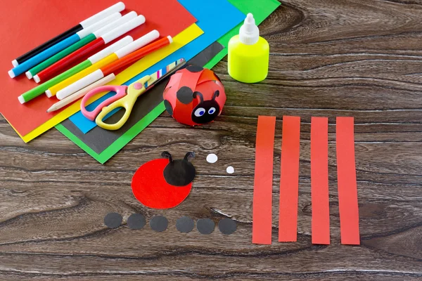 The child makes crafts out of paper ladybug. Glue, paper, scisso