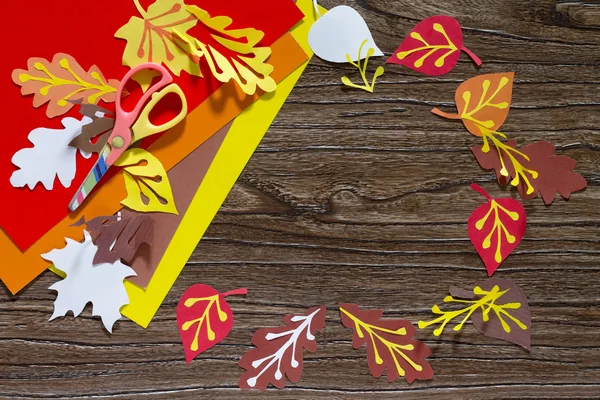 Autumn colored paper leaves on the wooden background. The sheet