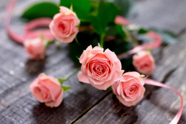 Beautiful pink roses on a dark wooden table with a pink ribbon