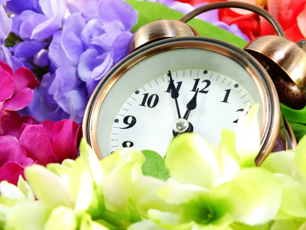 Spring time with alarm clock and artificial flowers bouquet background