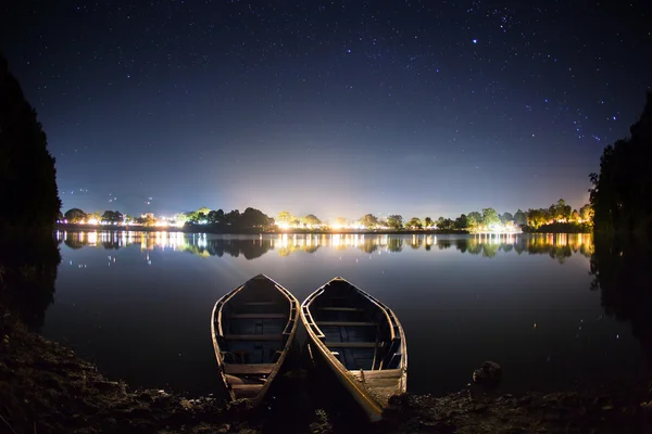 Two boats at the shore of a serene lake at night.