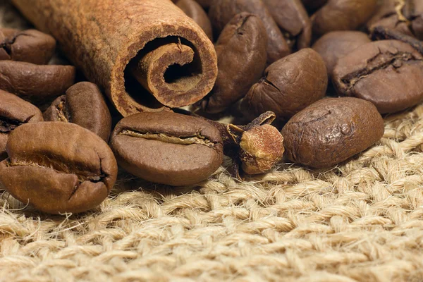 Roasted coffee beans with cinnamon stick and cloves flower close up on natural burlap