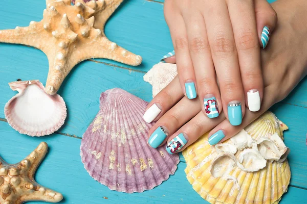 French manicure - beautiful manicured female hands with marine manicure with rhinestones on background seashells and starfish