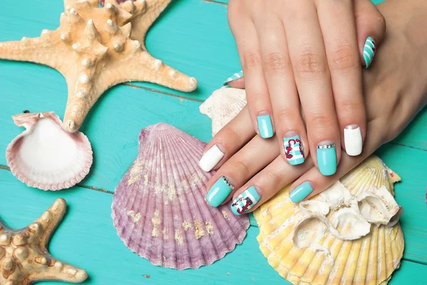 French manicure - beautiful manicured female hands with marine manicure with rhinestones on background seashells and starfish