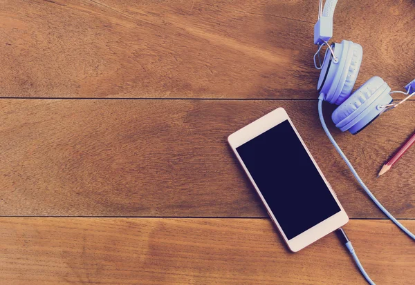 Smartphone or mobile phone,pen,note,blue headphones  on wood table.