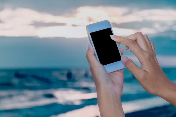 Hand holding mobile on low light beach background