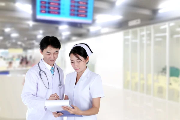 Doctor and nurse reviewing medical chart,  in hospital hallway